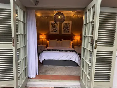 a bedroom with a bed with white sheets and windows at Pepler House in Franschhoek
