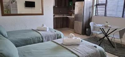 a room with two beds and a table and a kitchen at Cozy Quarters Self-Catering Accommodation in Bellville