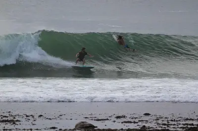 two people riding a wave on a surfboard in the ocean at Sea front holiday home in Bettyʼs Bay