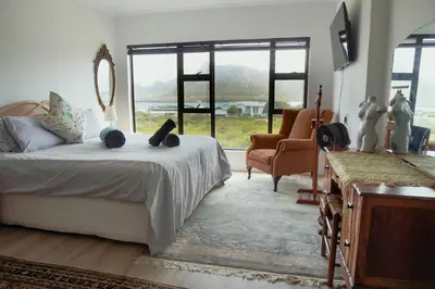 a bedroom with a bed and a chair and windows at Leah's View in Pringle Bay