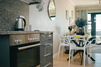 a kitchen with a stove and a table with chairs at Sea Facing 2 Bedroom Apartment In Burmeister On Park, Milnerton in Cape Town