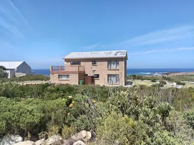 a house on a hill with the ocean in the background at Starfish - The rockpool house in Bettyʼs Bay