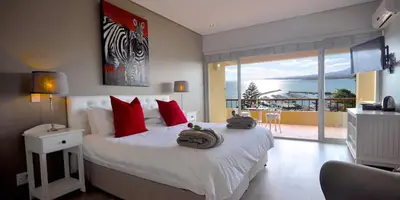 a bedroom with a bed with red pillows and a balcony at Celtic Manor Boutique Guest House in Gordonʼs Bay