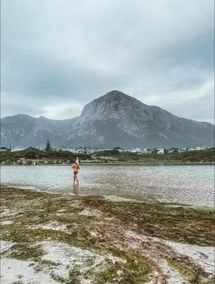 a person standing in the water with a mountain in the background at Pura Vida Hermanus in Hermanus