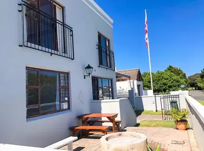 a white building with a picnic table and an american flag at Pura Vida Hermanus in Hermanus