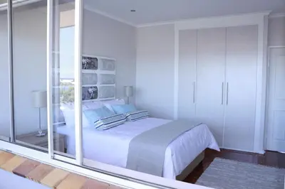 a white bedroom with a bed and a glass wall at Westward HO Apartment 13 in Cape Town