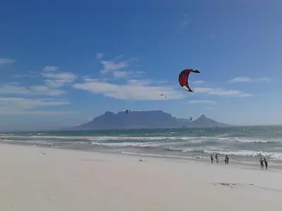 a group of people flying kites on the beach at Port House in Bloubergstrand