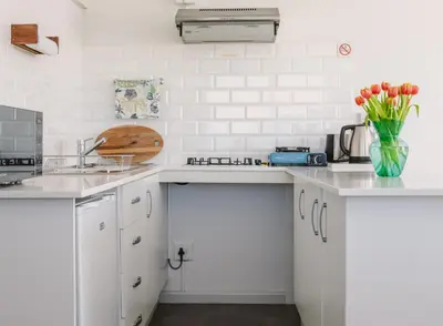 a white kitchen with white cabinets and a vase of flowers at Brookwood Cottage in Somerset West