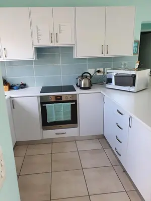 a kitchen with white cabinets and a stove and microwave at Sea and Mountain View Apartment in Gordonʼs Bay