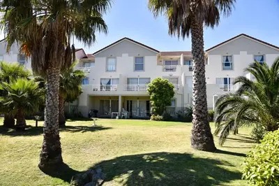 a large white building with palm trees in front of it at Sea and Mountain View Apartment in Gordonʼs Bay