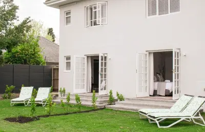 a white house with two chairs on the lawn at Rozenburg Guest House in Stellenbosch