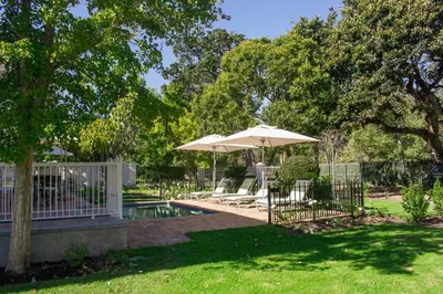 a patio with an umbrella and chairs and a pool at Rozenburg Guest House in Stellenbosch