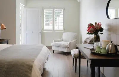 a bedroom with a bed and a table and a chair at Sugarbird Manor in Stellenbosch