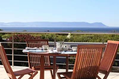 a wooden table and chairs on a balcony with the ocean at Abalone Guest Lodge in Hermanus