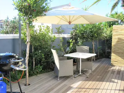 a patio with a table and an umbrella and a grill at OCEAN BREEZE SUNSET BEACH - Cape Town in Cape Town