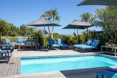 a swimming pool with blue chairs and umbrellas at Stay At Friends in Bettyʼs Bay
