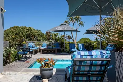 a swimming pool with blue chairs and an umbrella at Stay At Friends in Bettyʼs Bay