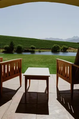 a table and two benches on a patio with a lake at ASARA Wine Estate & Hotel in Stellenbosch