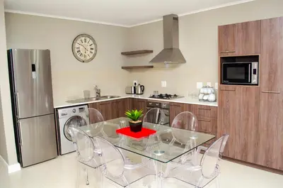 a kitchen with a glass table and chairs and a refrigerator at Mayfair Luxury Apartments in Cape Town