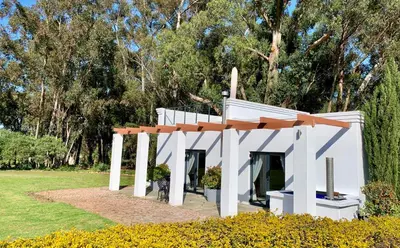 a white house in a park with trees in the background at Rest at Chabivin in Stellenbosch