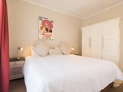 a bedroom with a white bed and a poster on the wall at 'Die Braaihuis'- sleeps 6, Large Veranda, Sea Views, Central and Fabulous! in Gordonʼs Bay