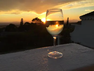 a glass of wine sitting on a table with the sunset at Montrose Guesthouse in Somerset West