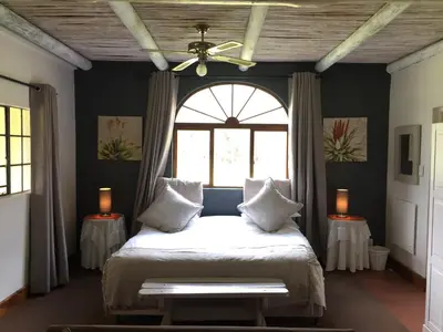 a bedroom with a bed with a ceiling fan and a window at Franschhoek Country Cottages in Franschhoek
