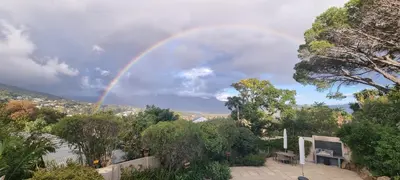a rainbow in the sky over a yard with trees at SomerZicht Guest House in Somerset West