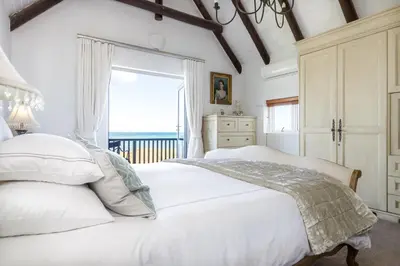 a white bedroom with a bed and a window at Strand Beach Lodge in Strand