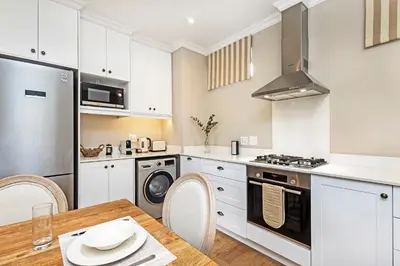 a kitchen with white cabinets and a wooden table with a dining room at L'ermitage - Franschhoek Chateau & Villas in Franschhoek