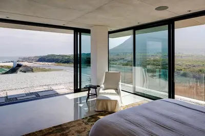 a bedroom with a bed and large glass windows at Restio River House in Pringle Bay