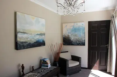 a room with a chair and paintings on the wall at Seaside Hermanus Guest Room in Hermanus