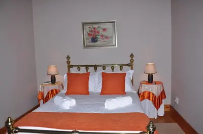 a bedroom with a bed with orange pillows and two lamps at Berg en Dal Guesthouse in Villiersdorp