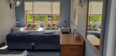 a bedroom with a bed and a desk and two windows at Cobie Apartment in Stellenbosch
