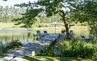 a dock with two chairs and an umbrella on a lake at Vredenhof Farm Cottage in Elgin