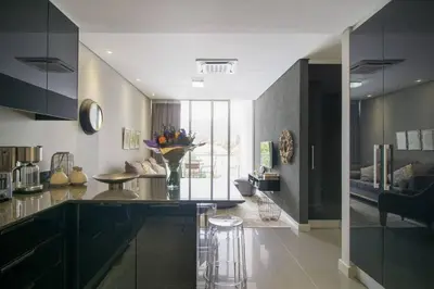 a kitchen with black cabinets and a living room at Lux Andringa Walk Apartments in Stellenbosch
