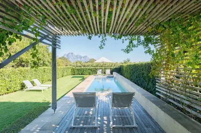 a swimming pool in the backyard of a house with a pergola at La Chataigne Wines & Guest Cottages in Franschhoek