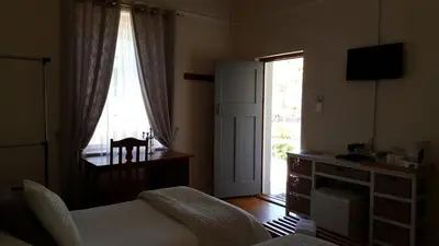 a bedroom with a bed and a desk and a window at Swartberg Guest House in Caledon