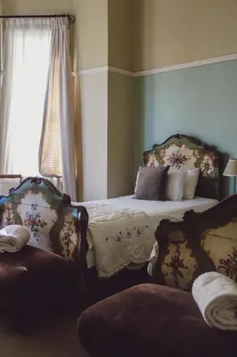 a bedroom with a bed with two chairs and a window at Pontac Manor Hotel & Restaurant in Paarl
