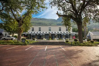 a large white building with trees and a brick parking lot at Pontac Manor Hotel & Restaurant in Paarl