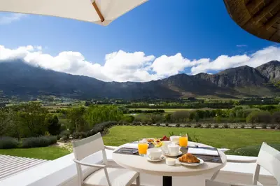 a table with food and drinks on a balcony with mountains at Mont Rochelle Hotel and Vineyard in Franschhoek