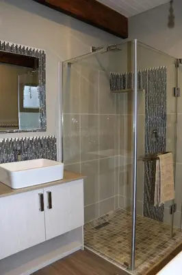 a bathroom with a shower with a sink and a mirror at Eagleview Guesthouse in Hermanus