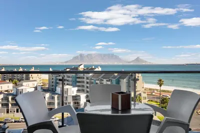 a table and chairs on a balcony with a view of the ocean at Aquarius Luxury Suites in Bloubergstrand