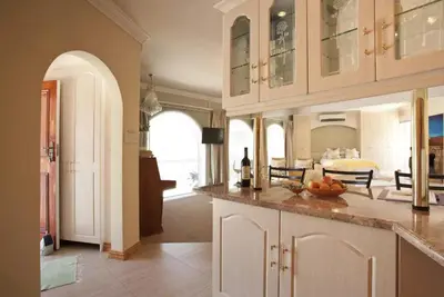 a kitchen with white cabinets and a living room at Somerset West Self Catering Vacation Rental - Experience the Best of Cape Town - Wine, Golf, Sea in Somerset West