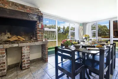 a living room with a fireplace and a table with chairs at Kingfisher Hollow in Gordonʼs Bay