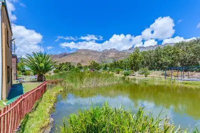a river next to a building with mountains in the background at Kingfisher Hollow in Gordonʼs Bay