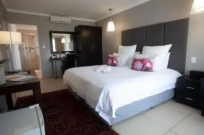 a bedroom with a large white bed and a desk at Ruslamere Hotel and Conference Centre in Durbanville