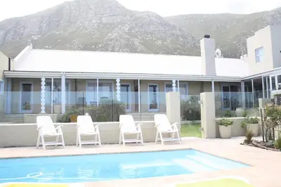 a house with a pool and white chairs and a house at Fijnbos Manor in Bettyʼs Bay