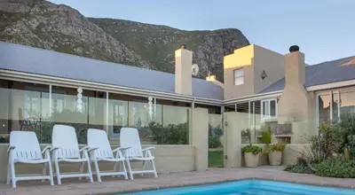 a group of white chairs sitting outside of a house at Fijnbos Manor in Bettyʼs Bay