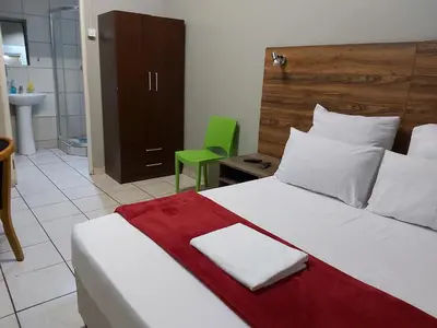 a bedroom with a large bed and a green chair at Hirondelle @ 45 Old Paarl in Bellville